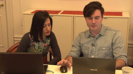 two people sitting at a table in the corporate world with laptops in front of them.