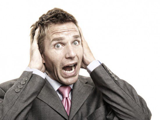 a man in a suit frantically covering his ears with his hands while surrounded by coworkers.